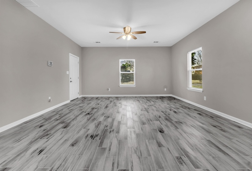 Spacious room featuring wood-finish flooring, two windows, a ceiling fan with integrated lighting, and neutral wall tones