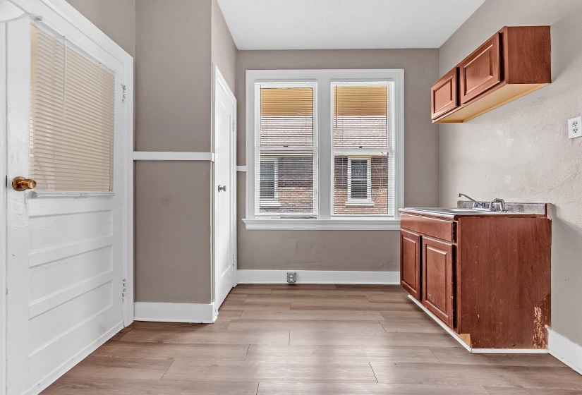 Kitchenette featuring wood-finish flooring, two large windows, a single-basin sink, and upper and lower cabinetry