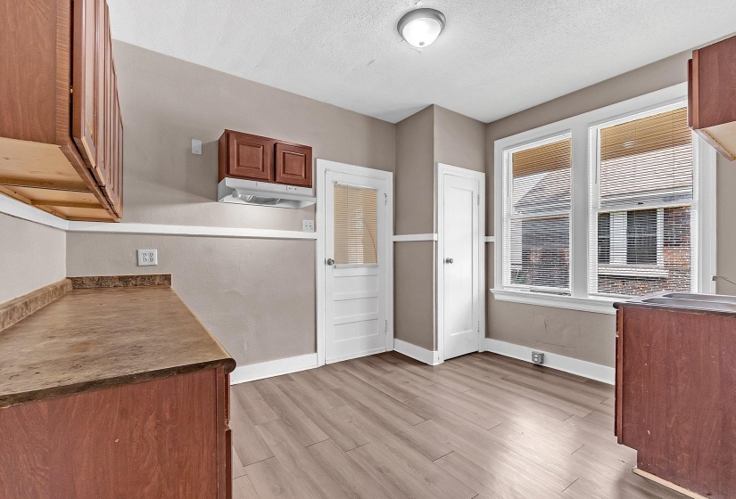 Kitchen space featuring wood-finish flooring, two windows with blinds, a white paneled door, and two-tone wall paint