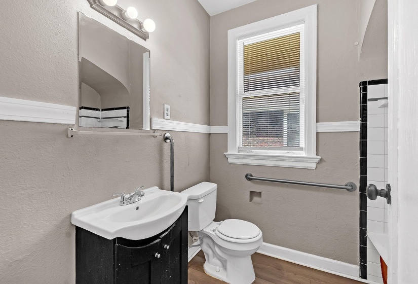 Bathroom featuring a dark wood-finish vanity with a white ceramic sink, a white toilet, and a window with blinds