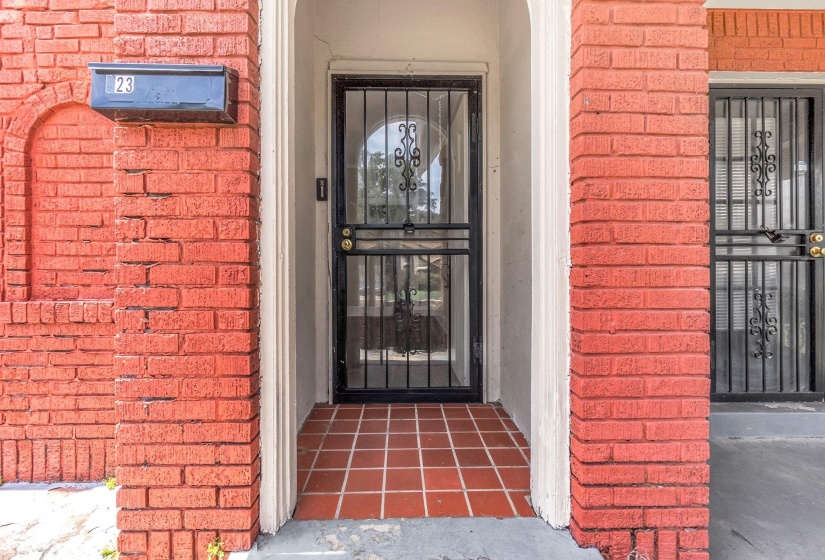 Red brick exterior featuring a security screen door, an arched alcove, and terra cotta tile flooring at the entry