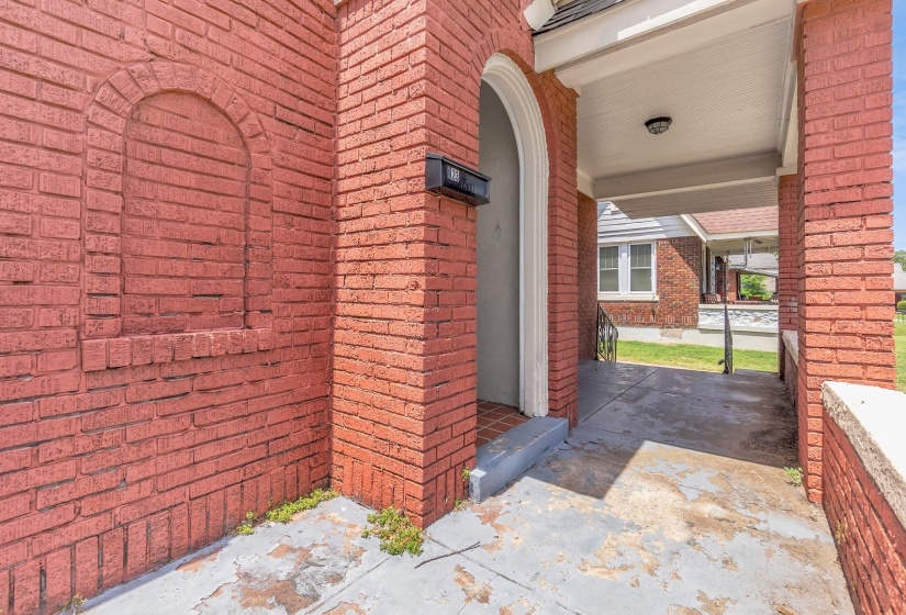 Brick exterior featuring an arched entryway, covered porch, and exterior lighting fixture
