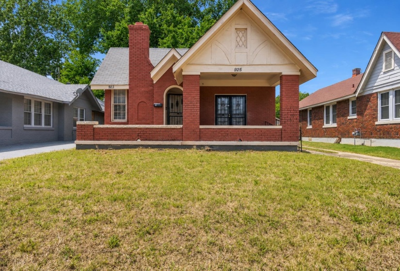 Brick exterior featuring a covered front porch with substantial columns, a prominent chimney, and a gabled roofline with decorative trim