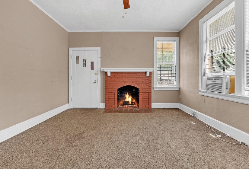 Living area featuring a brick fireplace with a white mantel, beige wall paint, white trim, and brown carpet flooring