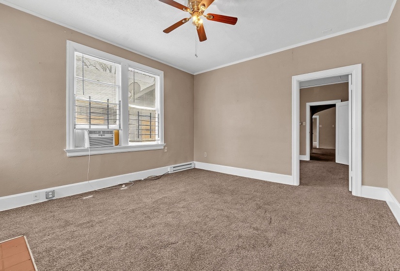 Spacious room with plush brown carpeting, a ceiling fan with wood-finish blades, and a white-trimmed window with horizontal blinds