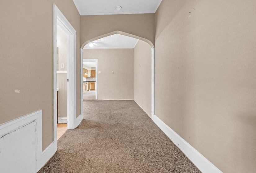 Carpeted hallway with neutral-toned walls, white baseboards, and a decorative arched doorway
