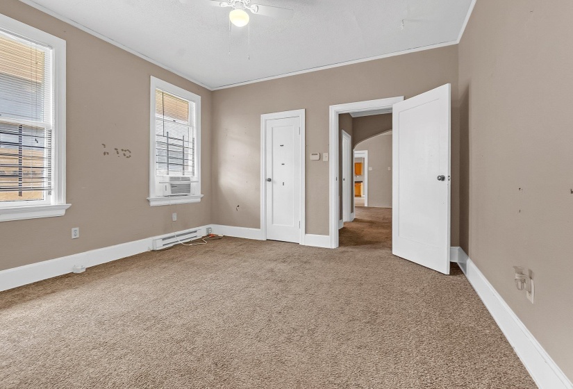 Carpeted room featuring two windows with blinds and security bars, a wall-mounted air conditioning unit, and a ceiling fan