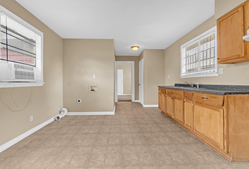 Kitchen area featuring tile flooring, wood-finish cabinetry, a dark countertop, and a double basin sink