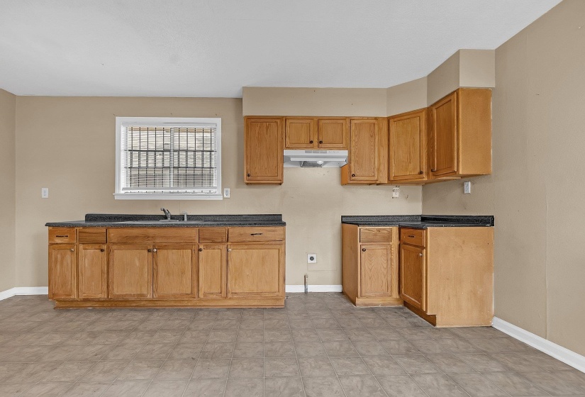 Kitchen featuring light wood cabinetry, dark countertops, and vinyl flooring