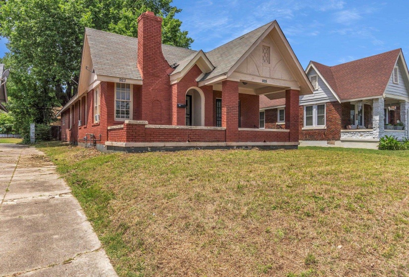 Brick exterior featuring a covered front porch with substantial columns, a prominent brick chimney, and a gabled roofline