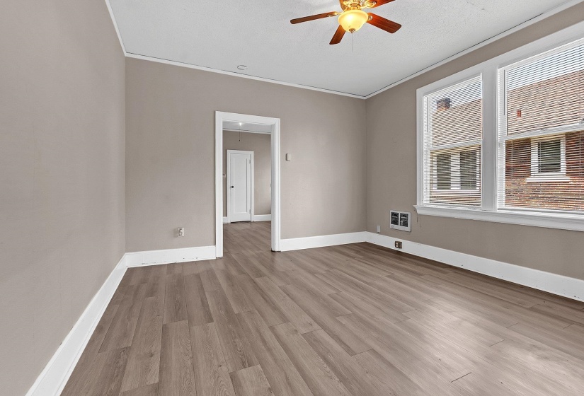 Spacious room featuring wood-finish flooring, neutral wall paint, white trim, and a ceiling fan