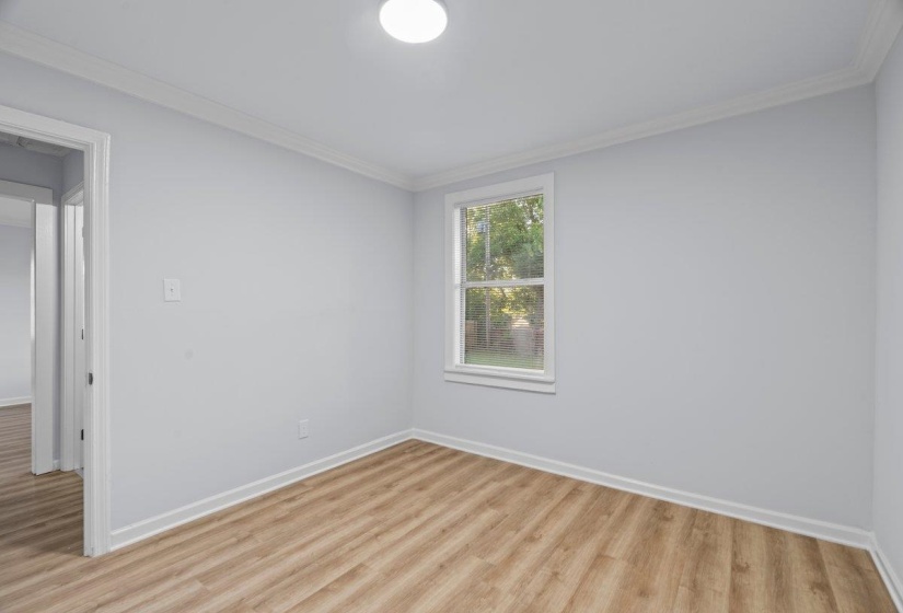 Room featuring wood-finish flooring, white baseboards, and crown molding