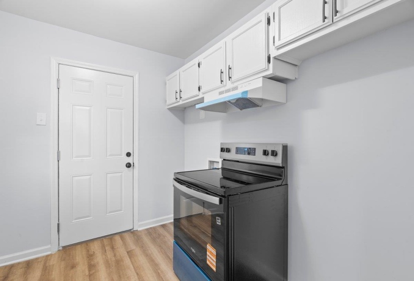 Kitchen area featuring wood-finish flooring, white paneled door, and light gray walls