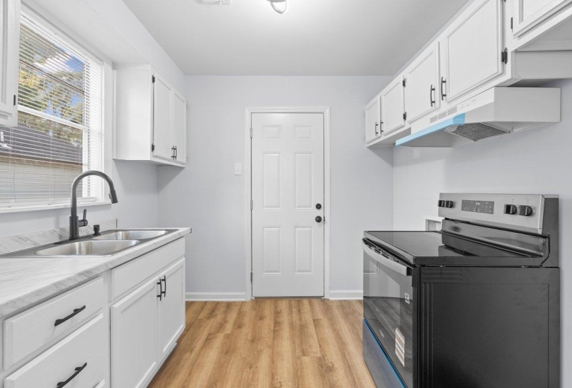 Updated kitchen featuring white shaker cabinetry, wood-finish flooring, white marble-look countertops, a dual-basin stainless steel sink with a matte black gooseneck faucet, and a black electric range with an overhead vent hood