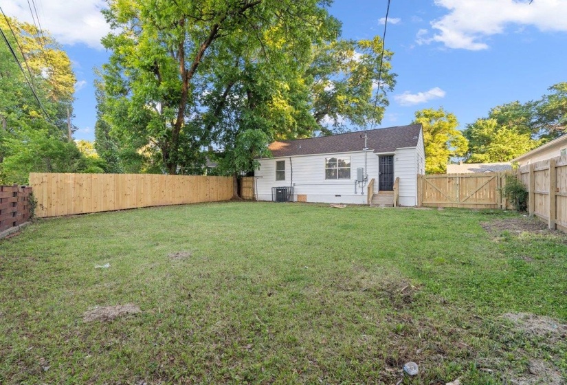 Expansive rear yard featuring a partial new wood privacy fence, a white exterior home with a dark roof, and a wooden rear deck with steps