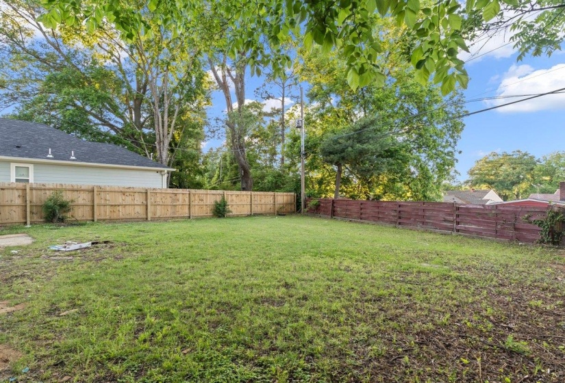 Expansive green space featuring a wood fence, mature perimeter trees, and a light-colored exterior wall