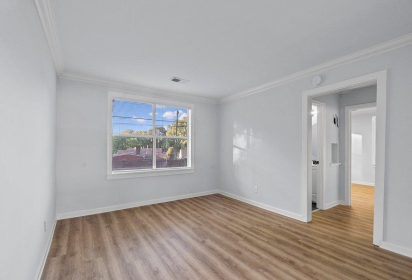 Spacious room featuring wood-finish flooring, light grey walls, and white crown molding
