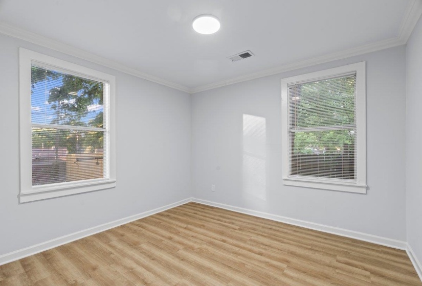 Interior room featuring two windows with blinds, wood-finish flooring, light gray walls, and white crown molding