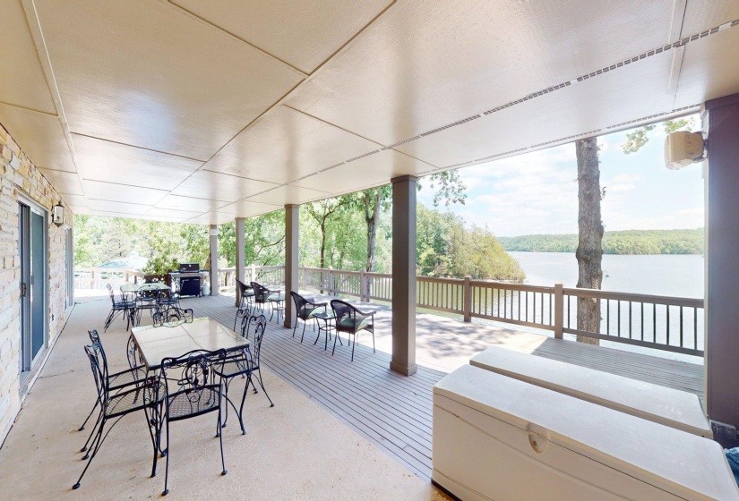 Covered outdoor patio with a stone-clad exterior wall, sliding glass doors, and a wood-finish deck with a railing