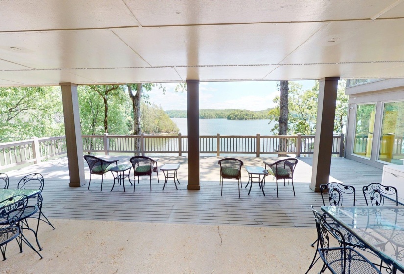 Expansive covered deck featuring a lake backdrop, wood-finish decking, and open-air railing