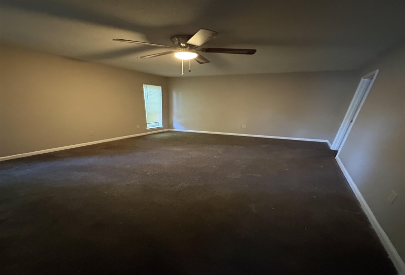 Spacious room featuring neutral-toned walls, dark carpeting, and a ceiling fan with integrated lighting