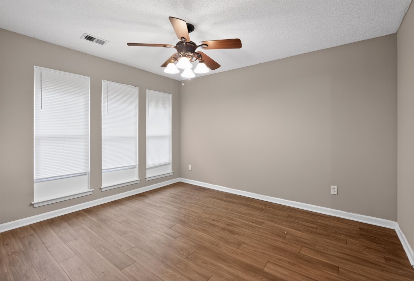 Spacious room featuring three windows with blinds, wood-finish flooring, a ceiling fan with integrated lighting, and neutral wall paint
