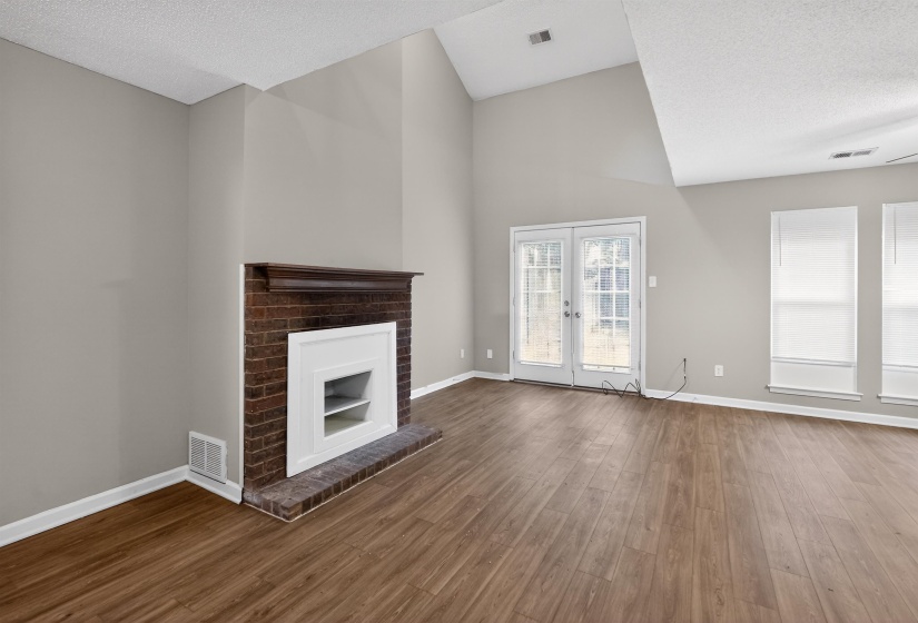Living area featuring a brick fireplace with white mantel, wood-finish flooring, and vaulted ceiling