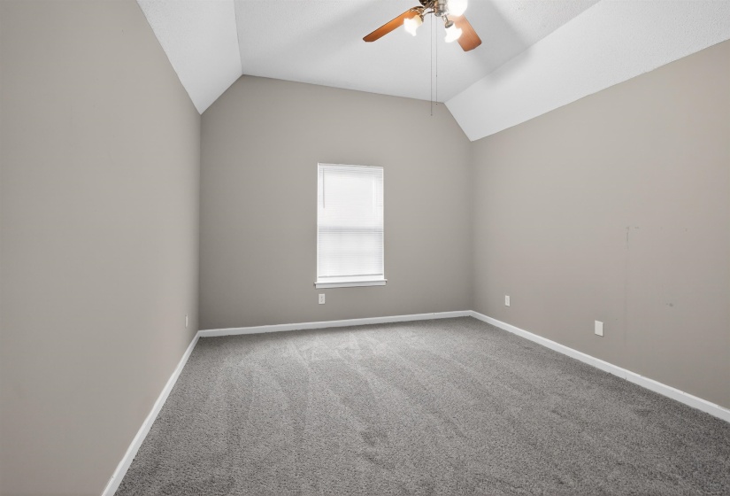 Room with vaulted ceilings, wall-to-wall carpeting, a single window with blinds, and a ceiling fan with light fixture