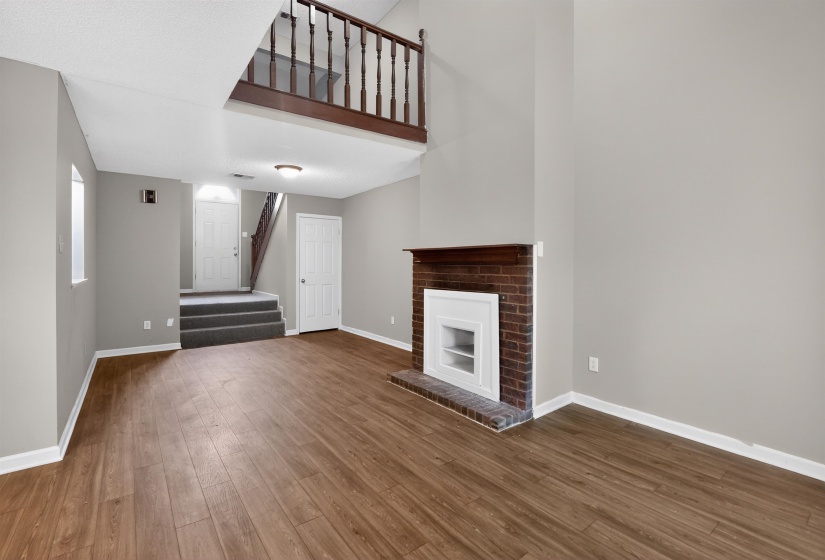 Spacious main living area featuring wood-finish flooring and a brick fireplace with a white mantel
