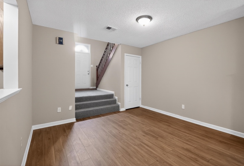 Open living area featuring wood-finish flooring, neutral-toned walls, and a recessed entryway with carpeted steps