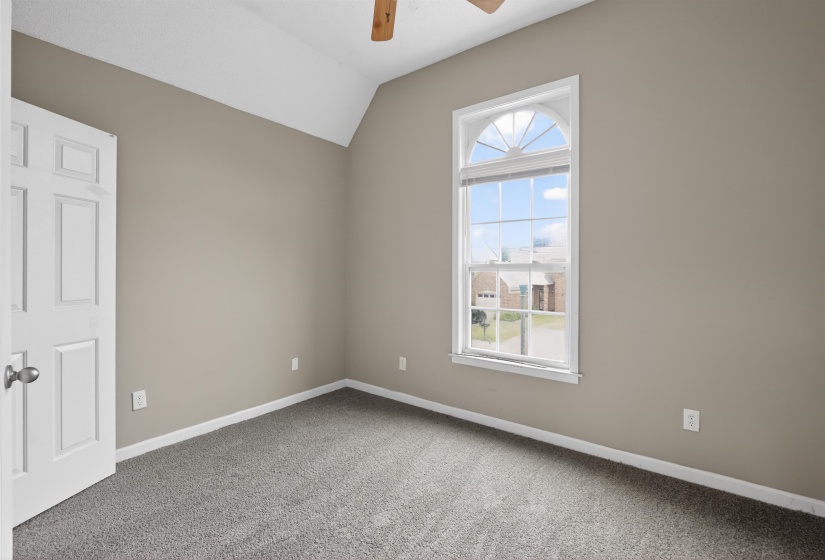 Room featuring vaulted ceilings, neutral wall tones, gray carpet flooring, an arched transom window, and a ceiling fan