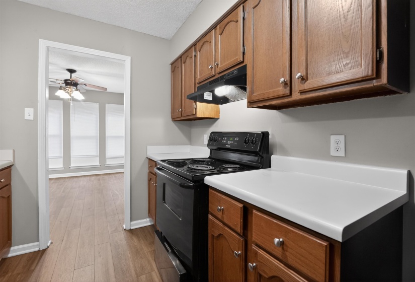 Kitchen featuring wood-finish cabinetry, white countertops, a black electric range, and wood-finish flooring