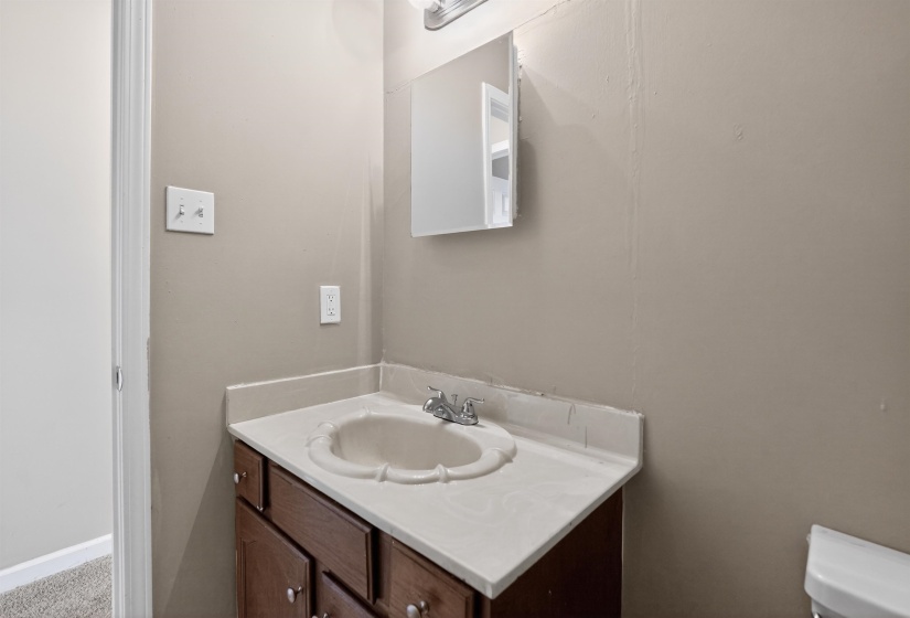 Bathroom vanity with a wood-finish cabinet, a white countertop, and an integrated sink