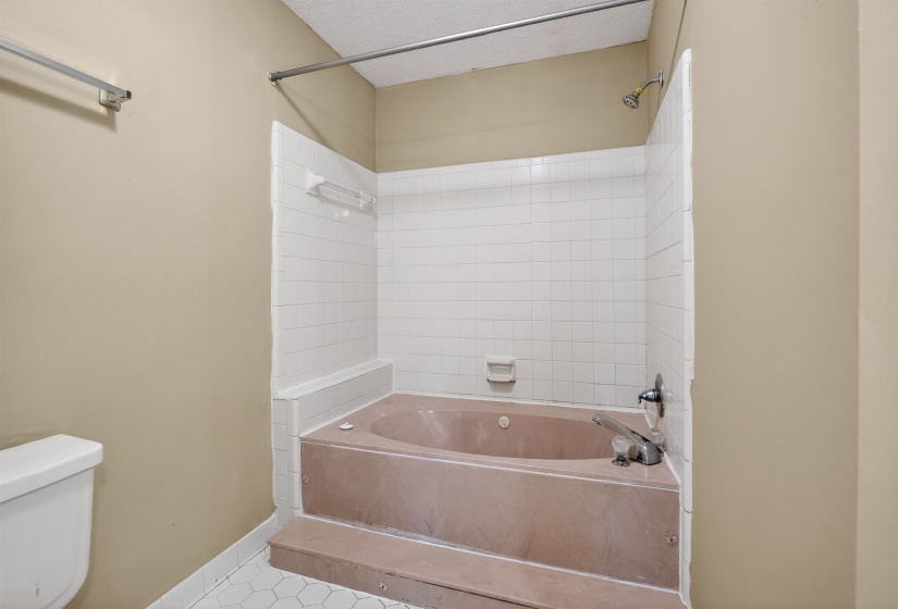 Built-in soaking tub with white subway tile surround, integrated shower fixture, and hexagonal floor tiling