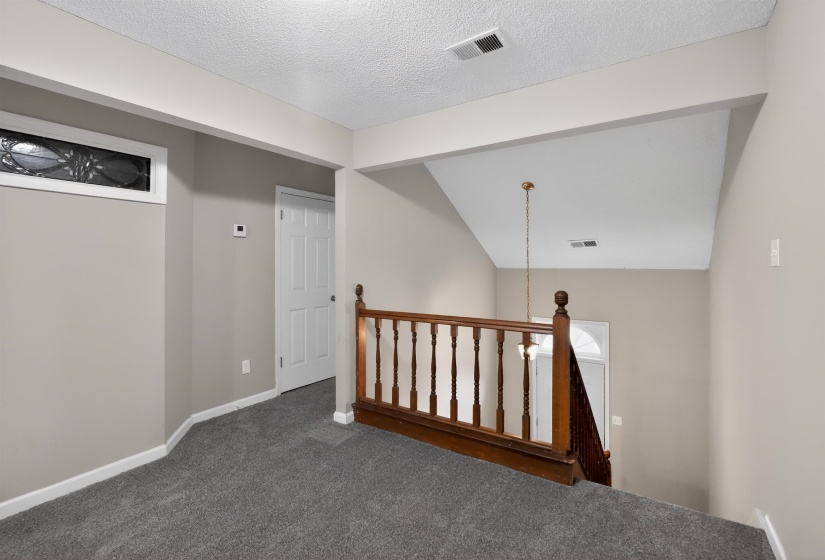 Carpeted upper-level landing featuring a wood-finish staircase railing and a decorative overhead light fixture