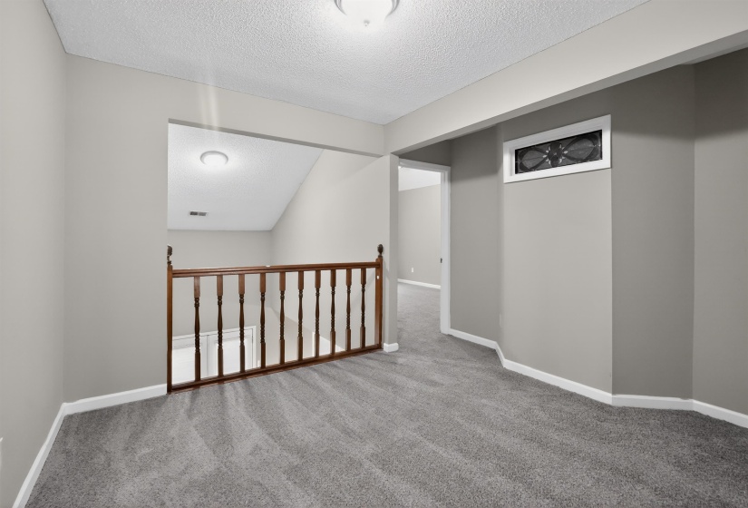 Carpeted upper-level landing featuring a wood-finish railing, neutral wall tones, and recessed lighting
