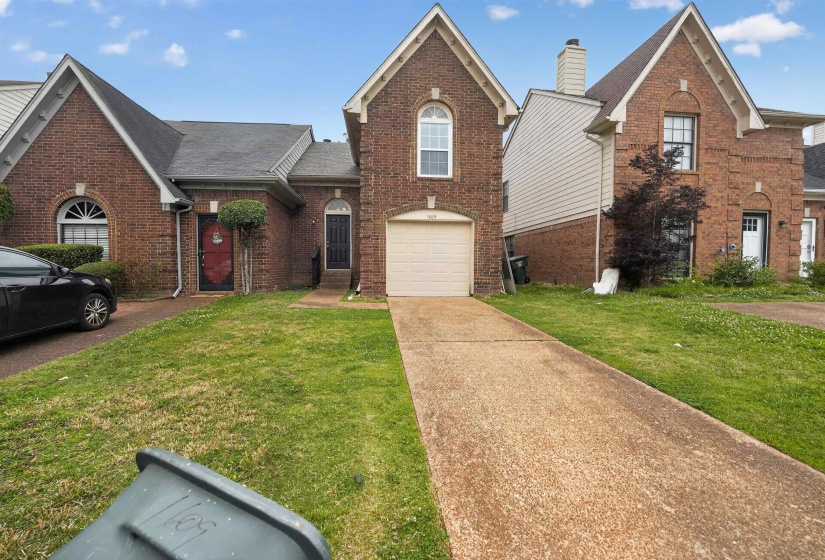 Brick exterior featuring a gabled roofline, arched windows, an attached garage, and a concrete driveway