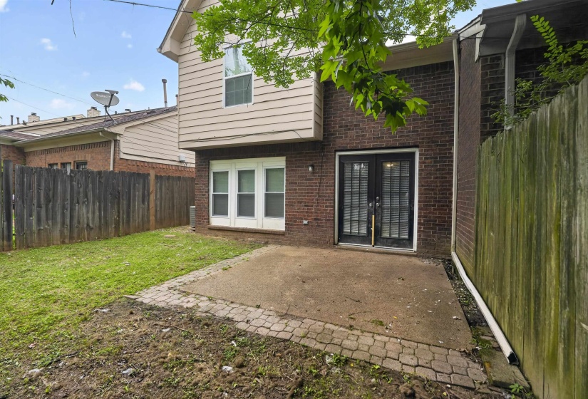 Private backyard featuring a brick and siding exterior, a concrete patio with paver accents, double glass-paneled doors, and perimeter fencing
