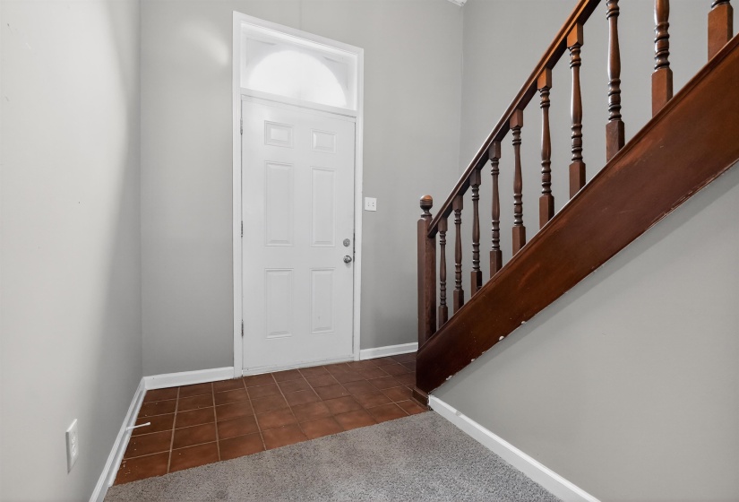Entryway featuring a paneled white door with an arched transom, brown tile flooring, gray wall paint, and a wood staircase with balusters