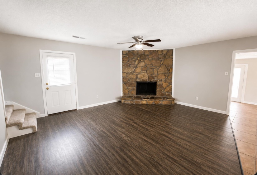 Living space featuring wood-finish flooring, a stone-faced fireplace with a hearth, a ceiling fan with integrated lighting, neutral wall paint, and a white door with integrated blinds