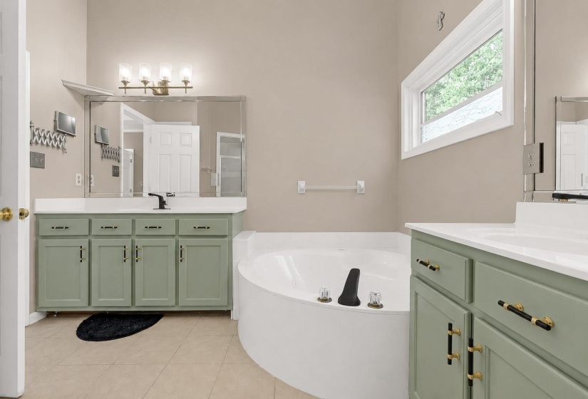 Bathroom featuring a corner soaking tub, two separate vanity sinks with light green cabinetry, and beige wall paint