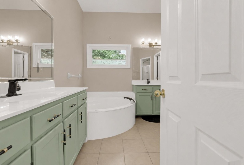 Bathroom featuring a large corner soaking tub, dual vanity with green cabinetry, white countertops, and tile flooring