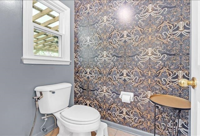 Powder room featuring a decorative wallpaper accent wall, light gray painted walls, and a white framed window