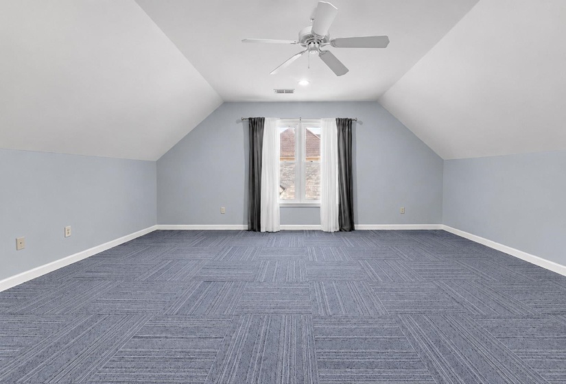 Spacious room featuring sloped ceilings, a centered window with drapes, and patterned carpet flooring