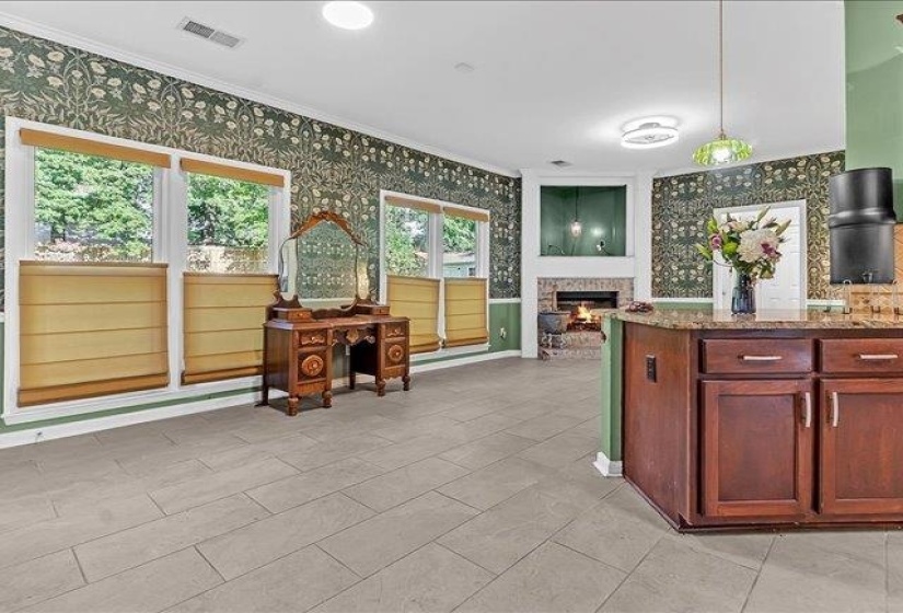 Expansive interior space featuring light-toned tile flooring, detailed patterned wallpaper, and a corner fireplace with a brick surround