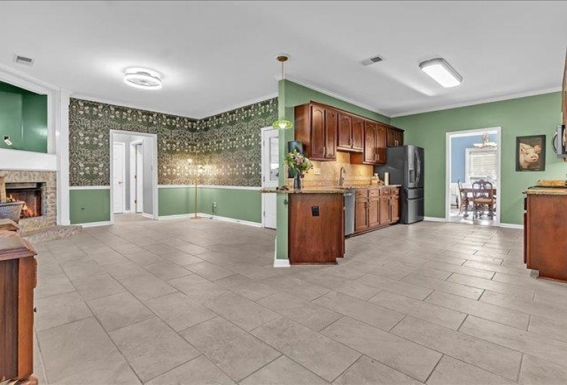 Expansive common area featuring large format tile flooring, a stone fireplace with hearth, and an open-concept kitchen