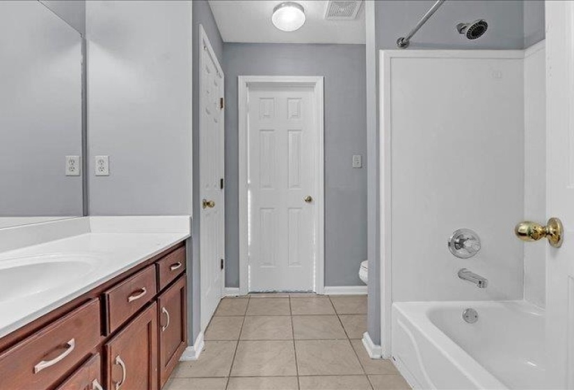 Bathroom featuring a single vanity with wood-finish cabinetry and a white countertop, large mirror, tile flooring, and a white bathtub with a shower fixture