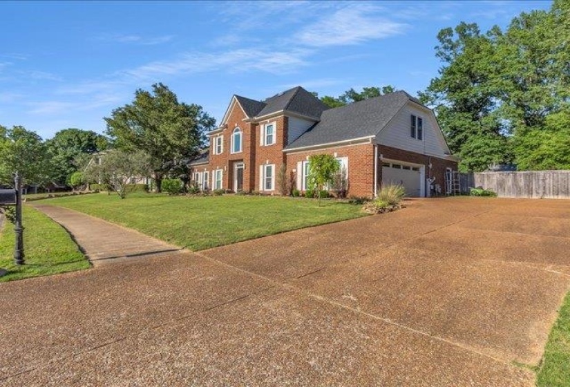 Brick facade residence featuring a two-car garage, mature landscaping, and a substantial driveway