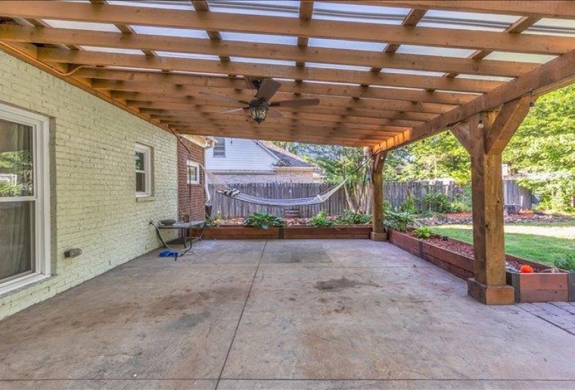 Expansive outdoor patio featuring a wood pergola with translucent roofing, a ceiling fan, and concrete flooring