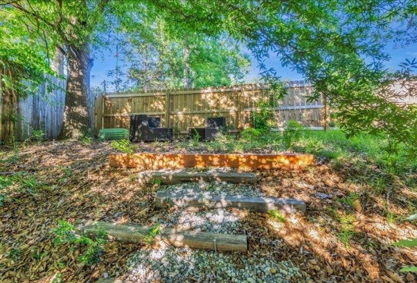 Tiered backyard featuring gravel steps, wood-edged garden beds, a wood privacy fence, and mature trees